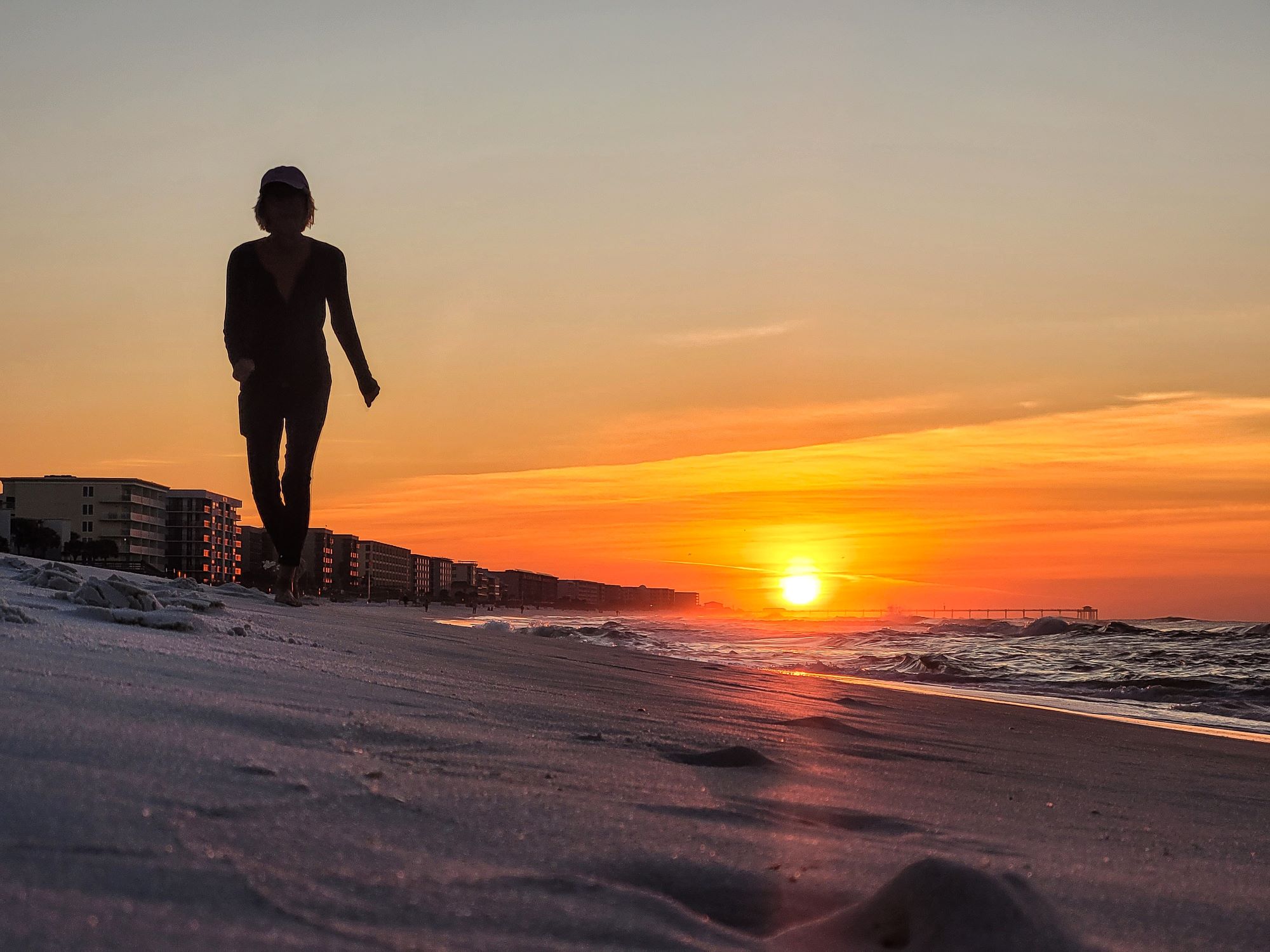 silhouetted woman walking down a beach during sunrise
