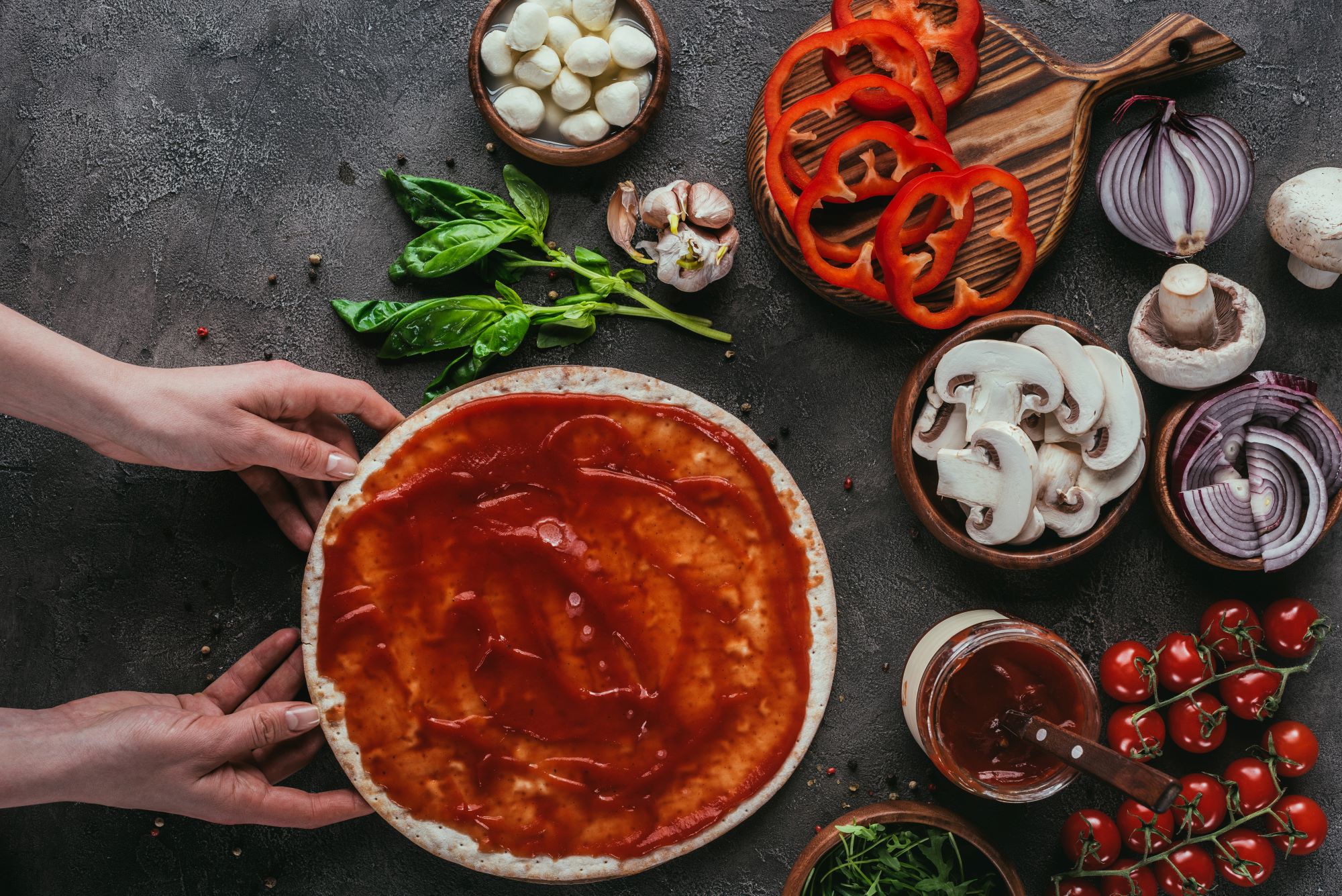a flat lay image of pizza dough with sauce on top, surrounded by colorful vegetables that will be used as toppings